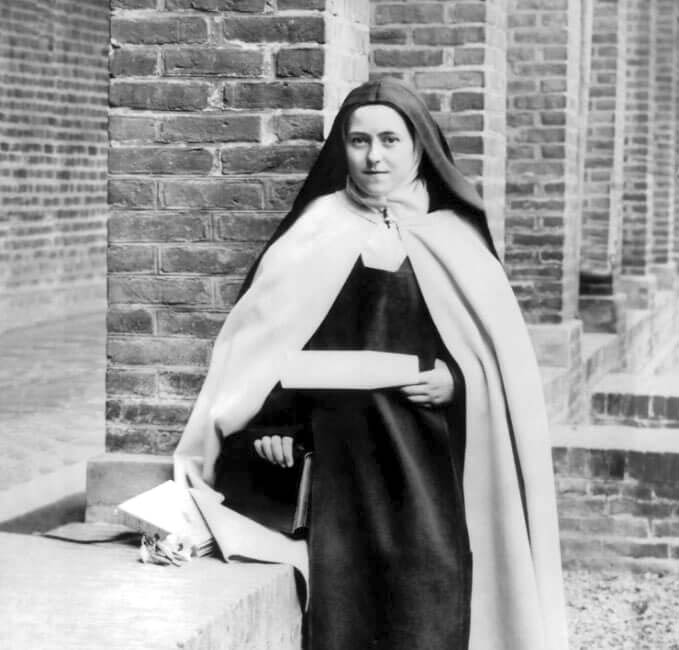 Photograph of Saint Thérèse of Lisieux in the Carmel courtyard, holding a parchment